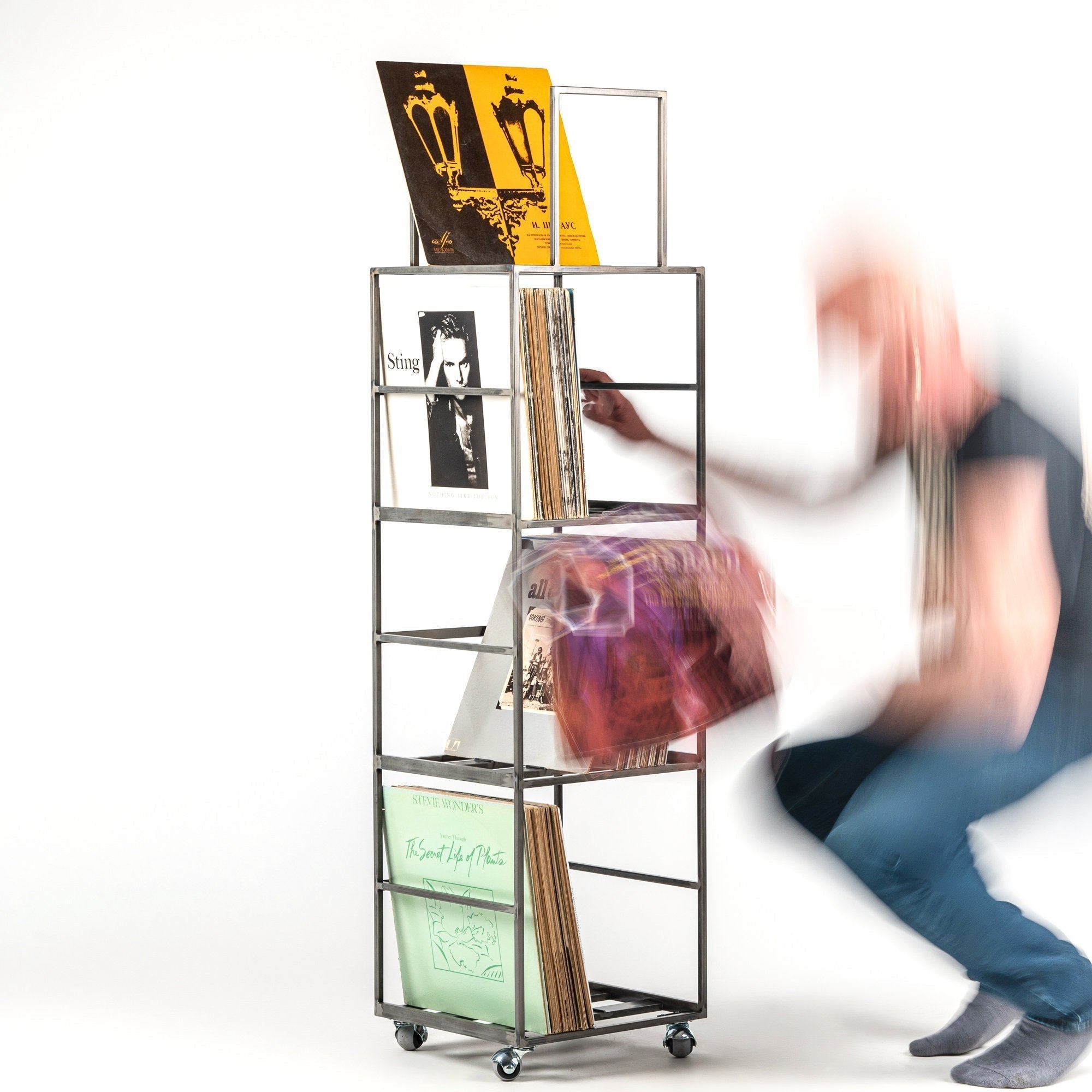 Four-tier metal vinyl record stand on wheels filled with LP records — a person browsing the collection