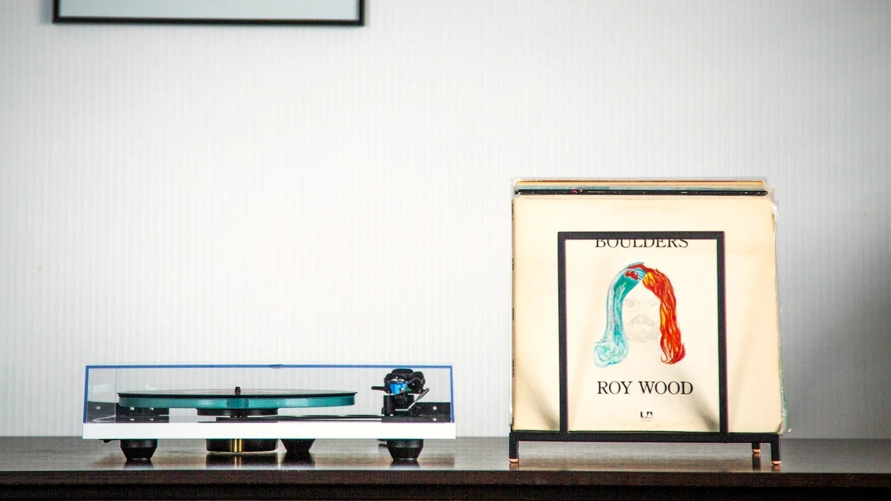 Turntable and an LP in a slim steel display stand on a dark console.