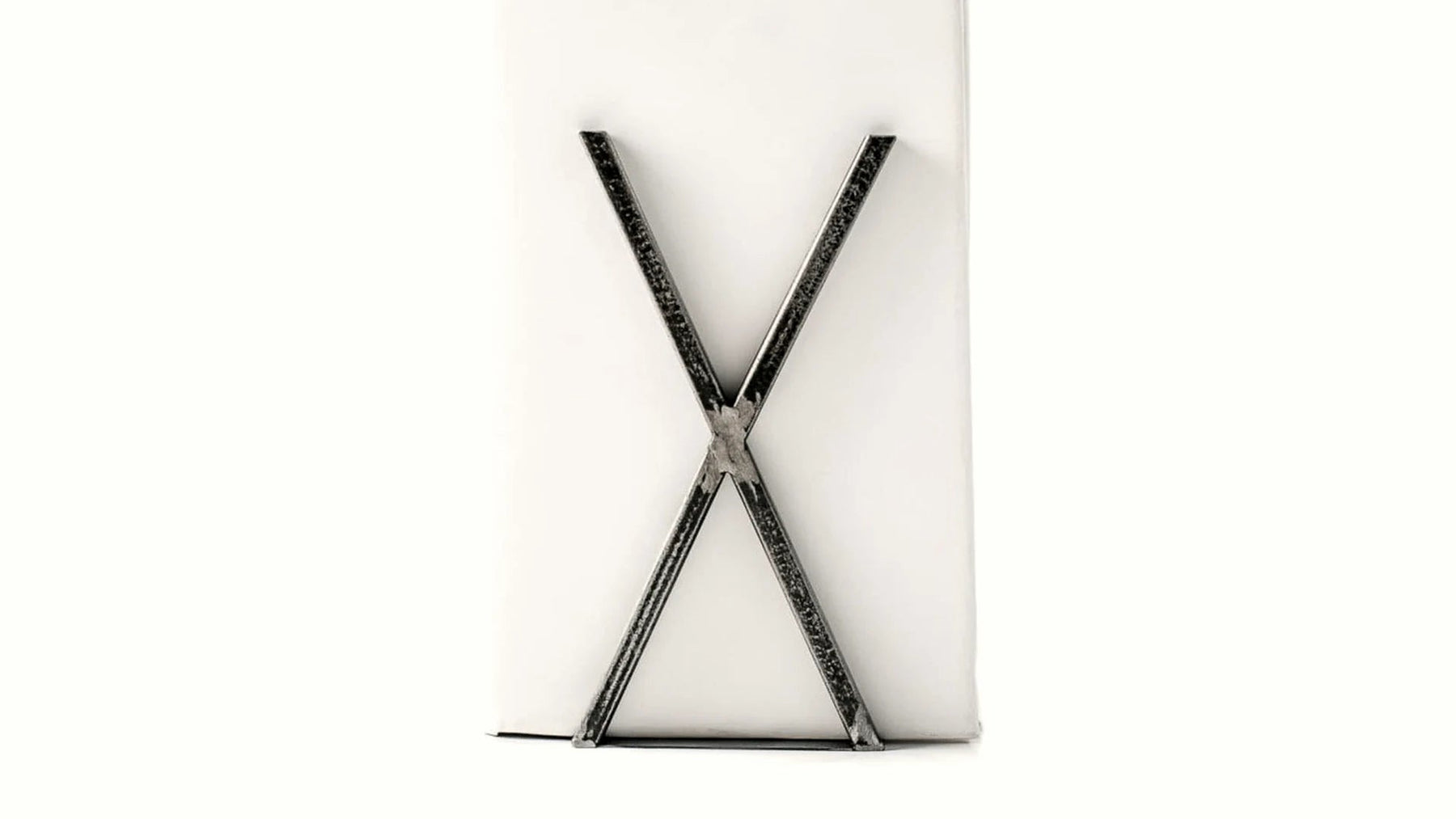 X-shaped hand-forged steel bookends supporting a white book.