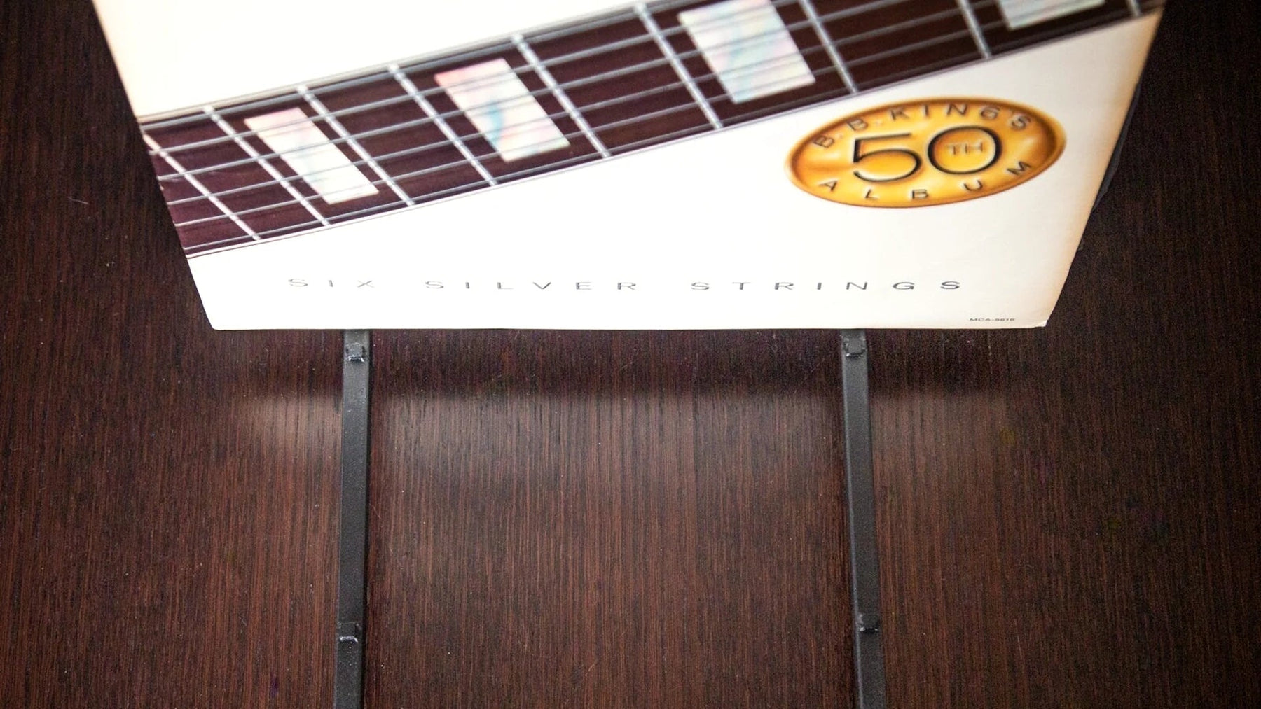 LP record on a steel stand on a dark wooden shelf.