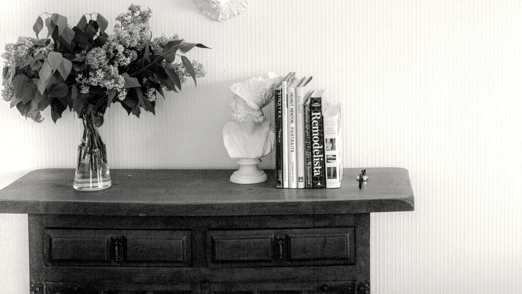 Plaster busts, books and dried flowers styled on a dark console table.