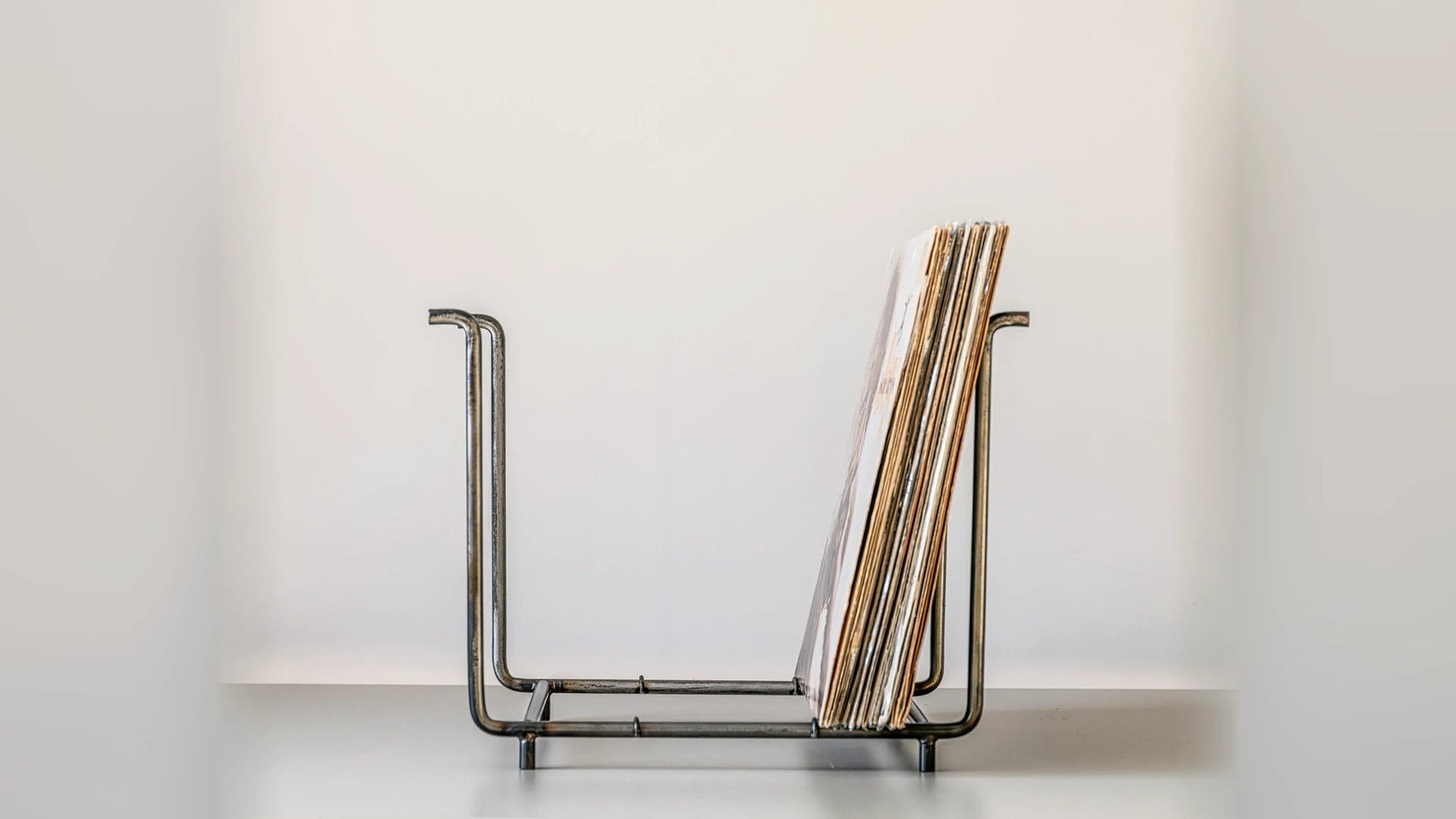 Low steel record rack holding a few LPs against a plain wall.