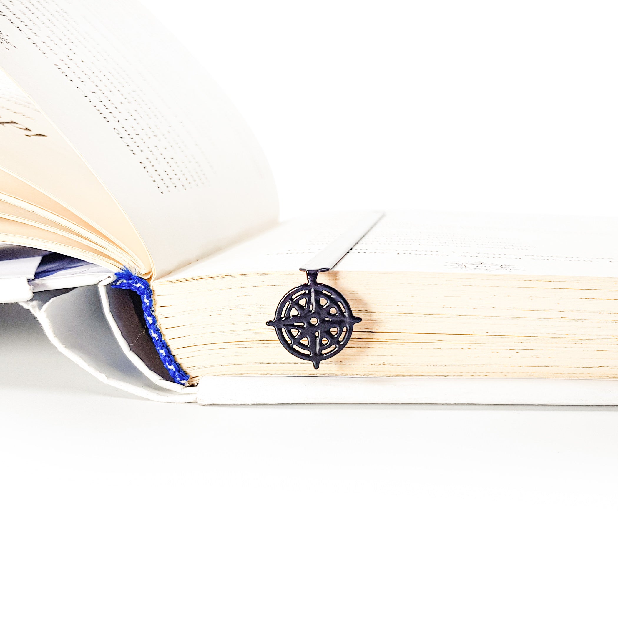 Compass rose metal bookmark nested in edge of thick open book, showing slim profile in use