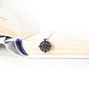 Compass rose metal bookmark nested in edge of thick open book, showing slim profile in use
