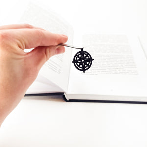 Hand holding compass rose bookmark over open book, showing full 6.7-inch length against text pages