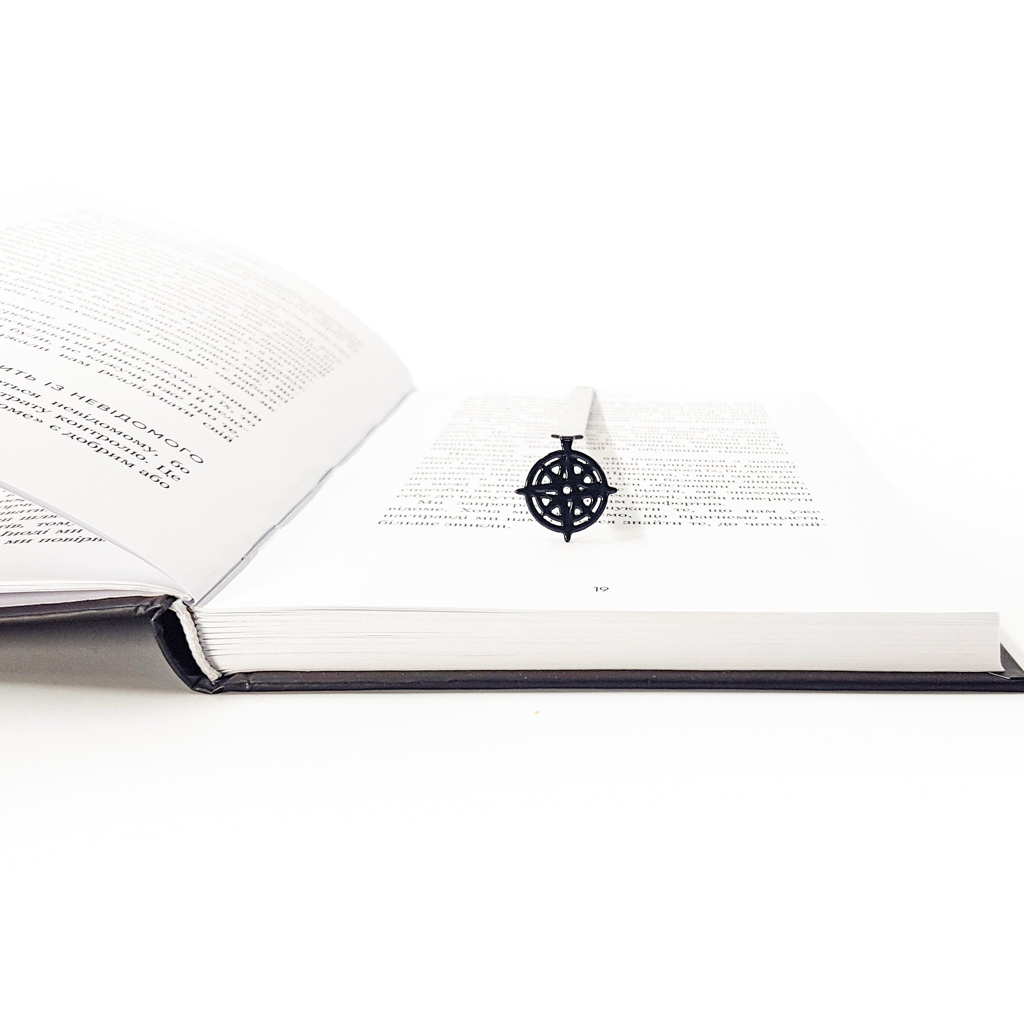 Compass rose metal bookmark resting across open book at angle, pendant centered on page