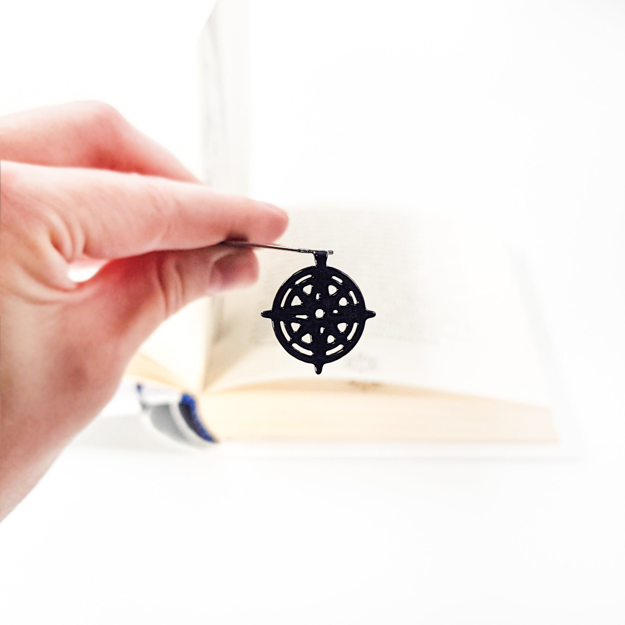Close-up of openwork compass rose pendant held between fingers, book blurred in background