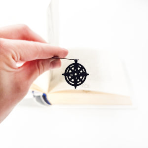 Close-up of openwork compass rose pendant held between fingers, book blurred in background