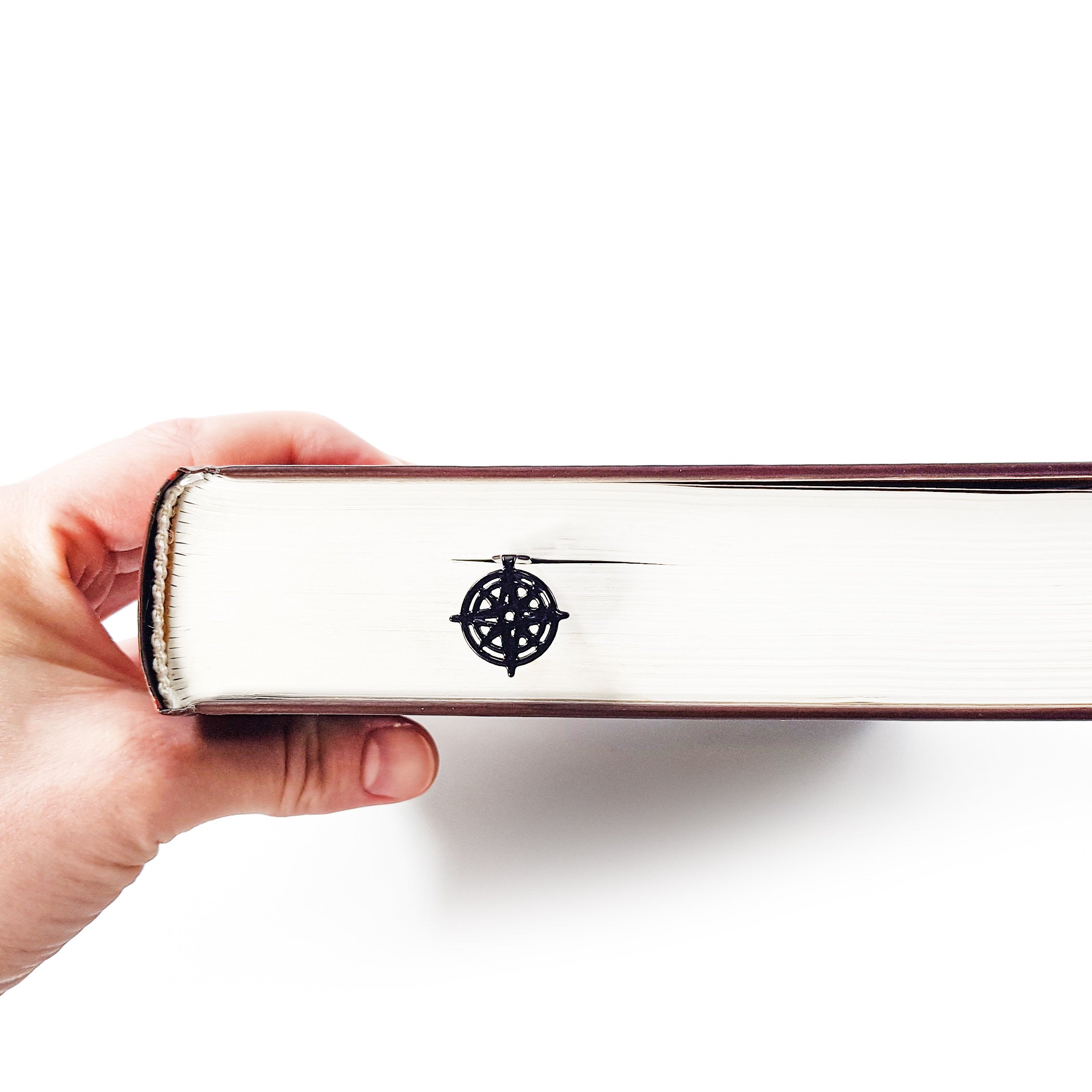 Compass rose bookmark protruding from closed book pages, hand holding book from side