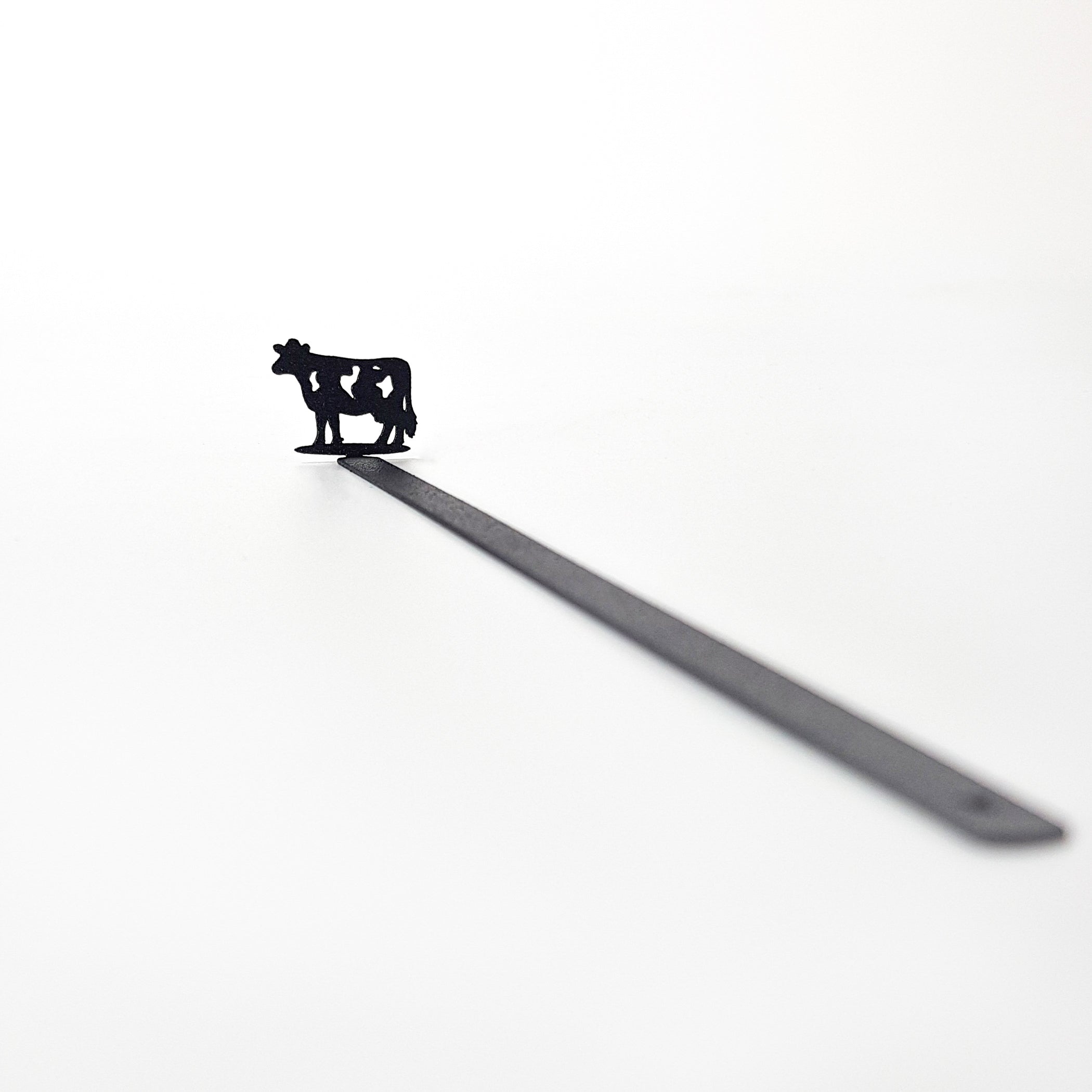 Full product shot — 17 cm laser-cut black steel cow bookmark on white background, diagonal view