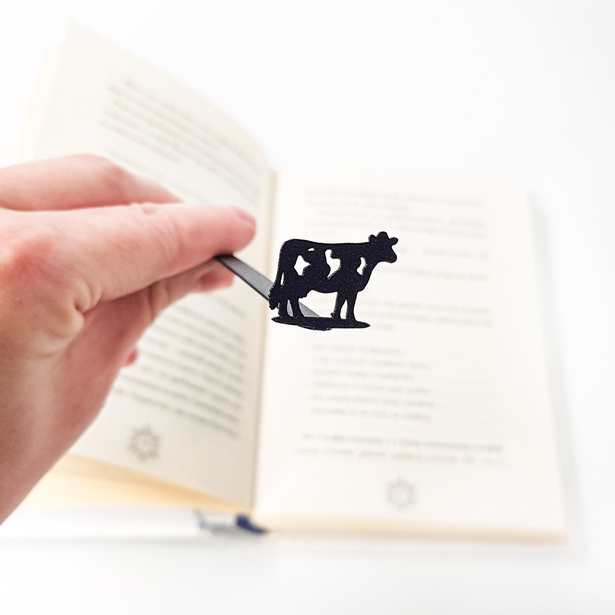 Metal cow bookmark in children's book, cow figure visible above illustrated page spread