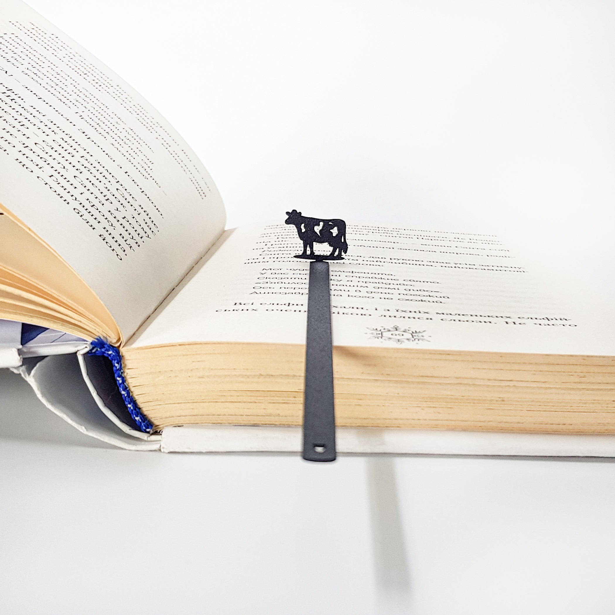 Black steel cow bookmark clipped to page corner, 0.6 mm blade visible from edge