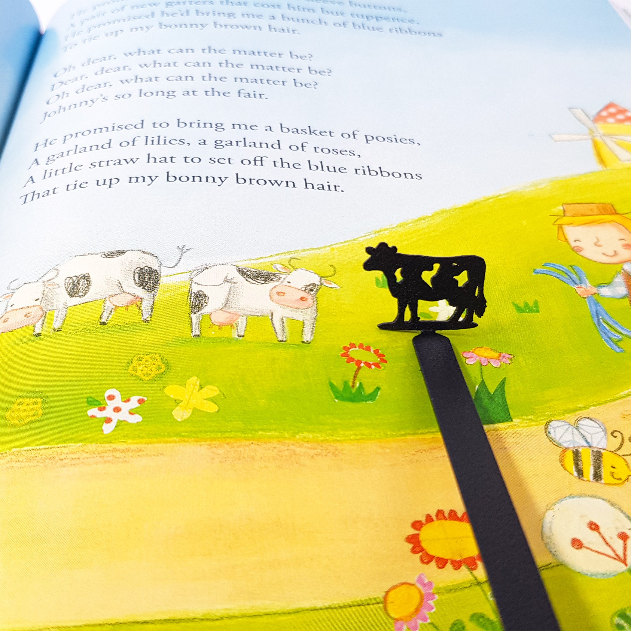 Close-up of laser-cut cow silhouette bookmark above pastoral children's book illustration