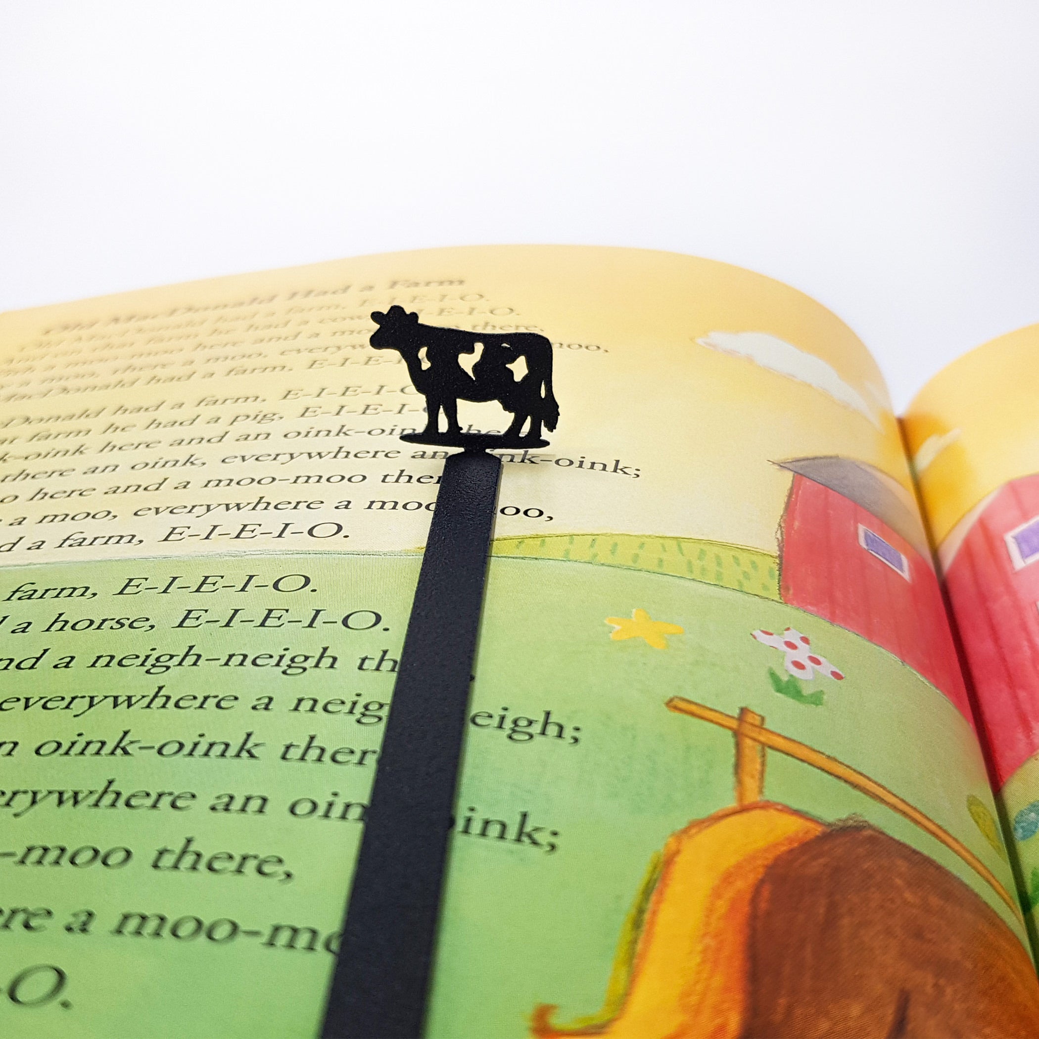 Top-down close-up of metal cow bookmark silhouette in open children's farm story book