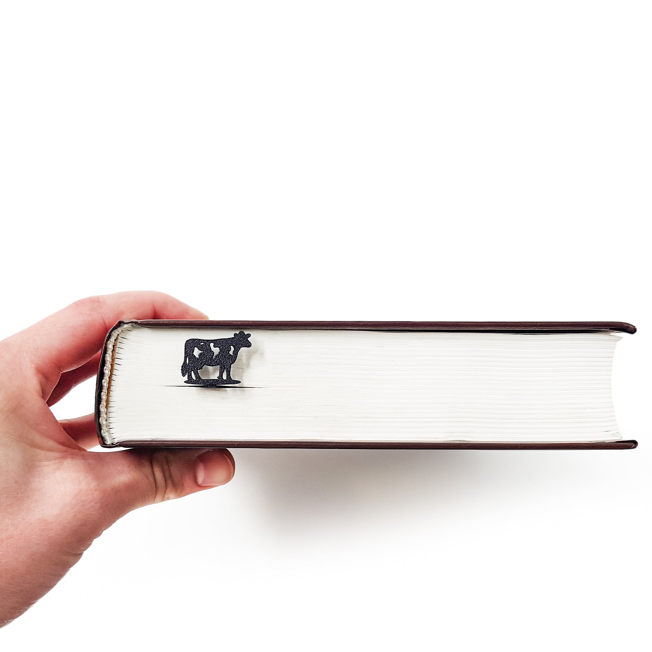 Metal cow bookmark clipped over page corner in open book, side angle view