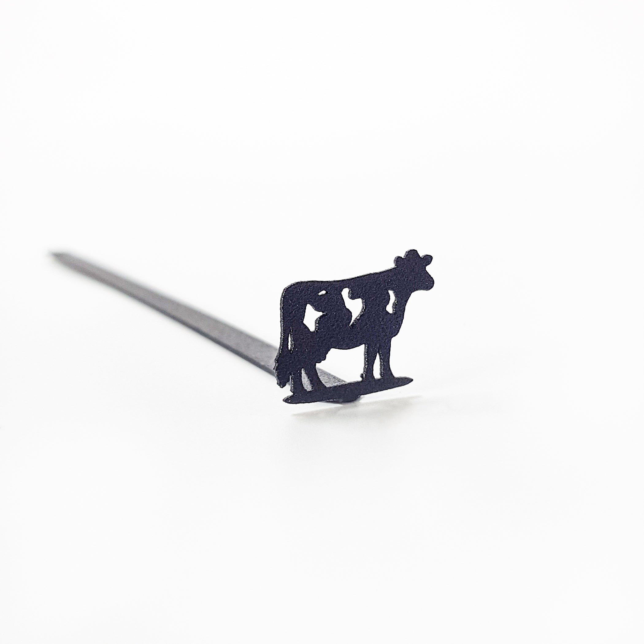 Black steel cow bookmark resting on closed book, product detail on neutral background