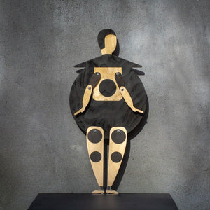 Bauhaus Beetle wooden marionette puppet standing on a black shelf against a grey wall, front view