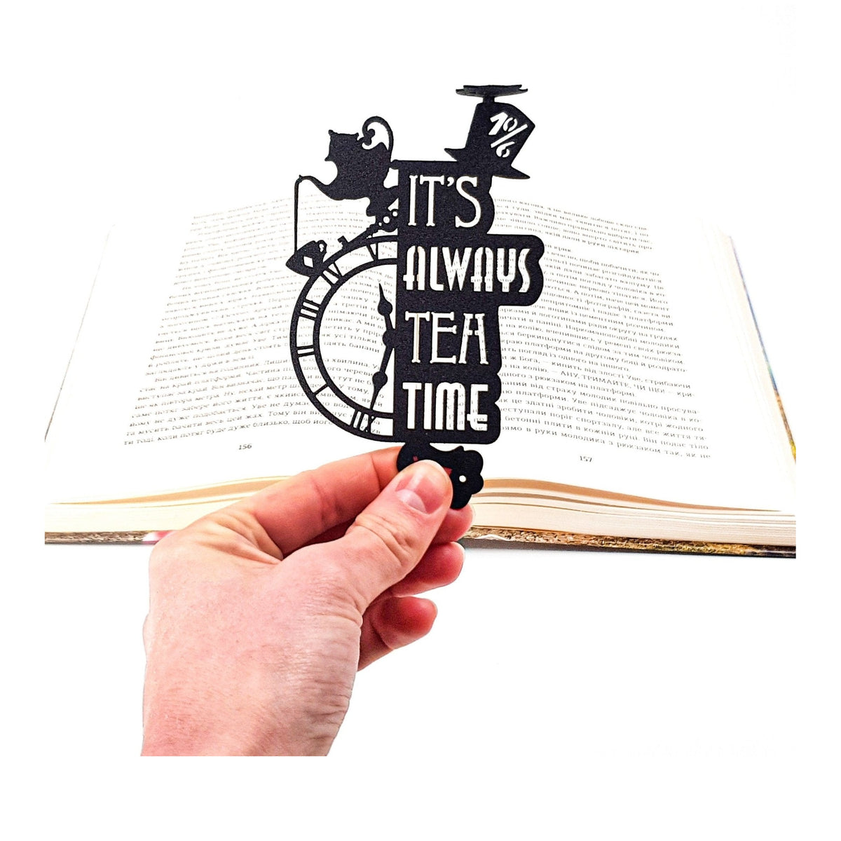 Alice in Wonderland's The Tea Party metal bookmark held in a hand above an open book