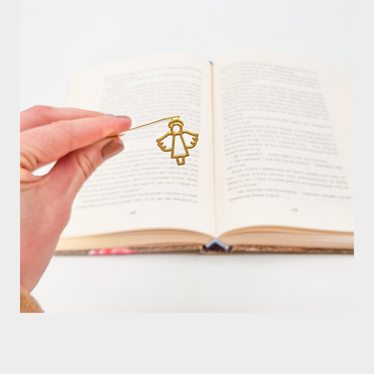 Angel metal bookmark in gold held in a hand above an open book