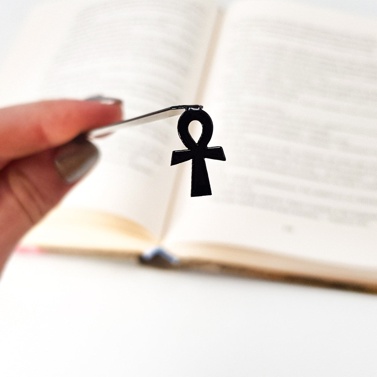 Ankh metal bookmark held in a hand above an open book