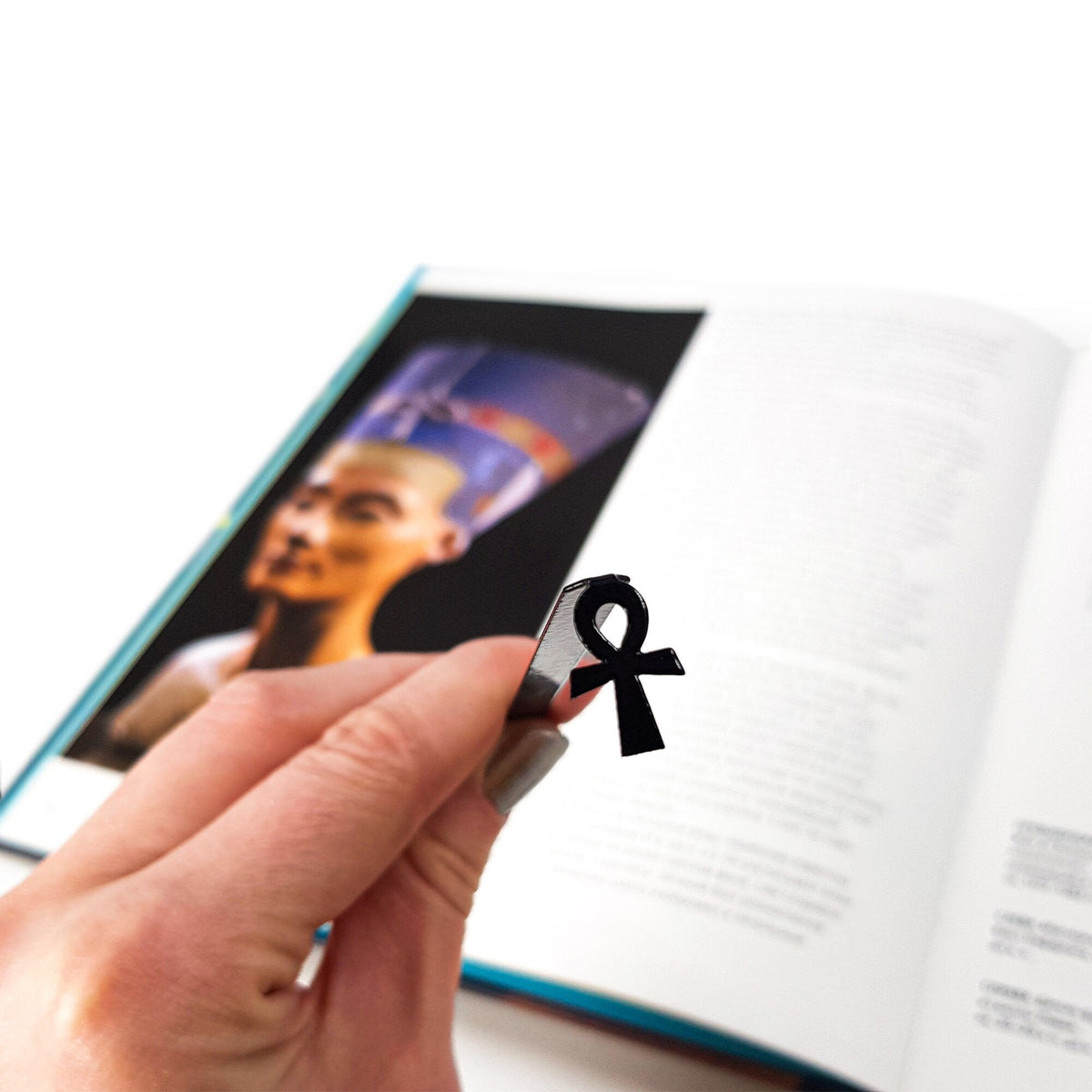 Ankh metal bookmark marking a page in an illustrated book, view 4