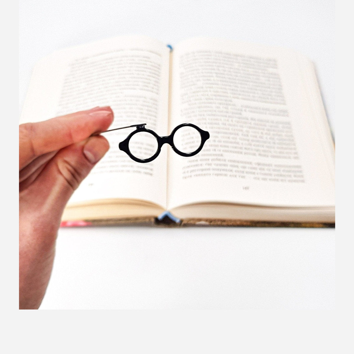 Architect's Eyeglasses metal bookmark held in a hand above an open book