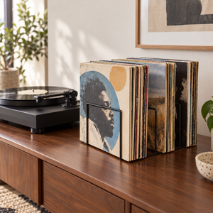 Black COMB wire-frame vinyl record stand holding upright LPs on a walnut cabinet beside a turntable.