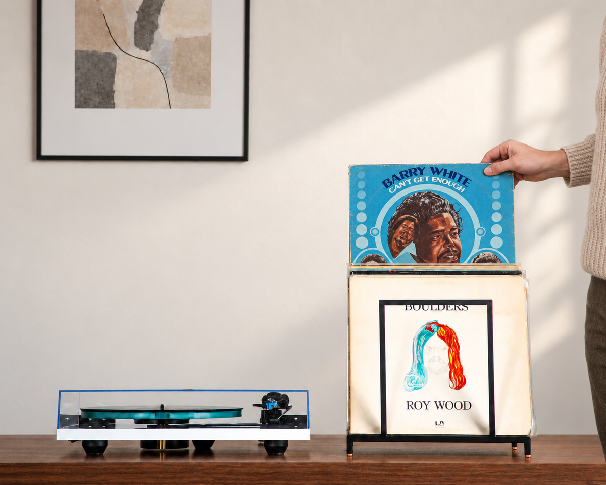 Person lifting a Barry White LP from a black desktop vinyl record stand with copper feet beside a turntable.