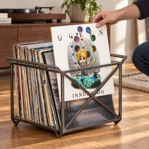 A person lifts a Queen Innuendo LP sleeve from an Atelier Article steel record crate with side handles and X-shaped braces beside a turntable.
