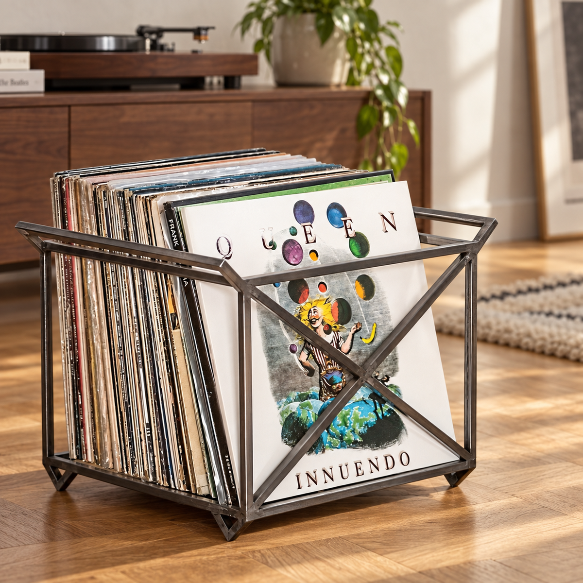Atelier Article steel vinyl record crate with side handles and X-shaped braces, holding Queen Innuendo and other LPs beside a turntable.