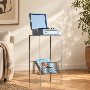 Atelier Article raw steel record player stand with a blue suitcase turntable and LPs in the lower wire basket beside a linen armchair