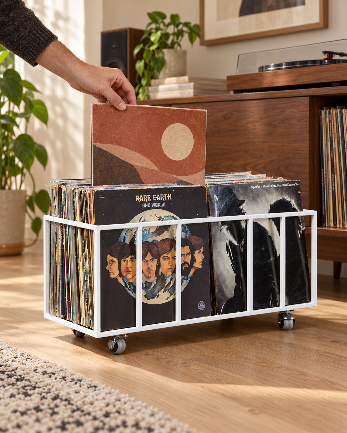 Hand selecting a vinyl record from the left row of a white Atelier Article TWINS two-row record crate on wheels beside a turntable.