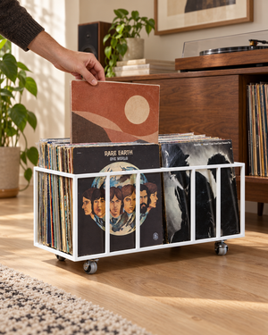Hand selecting a vinyl record from the left row of a white Atelier Article TWINS two-row record crate on wheels beside a turntable.
