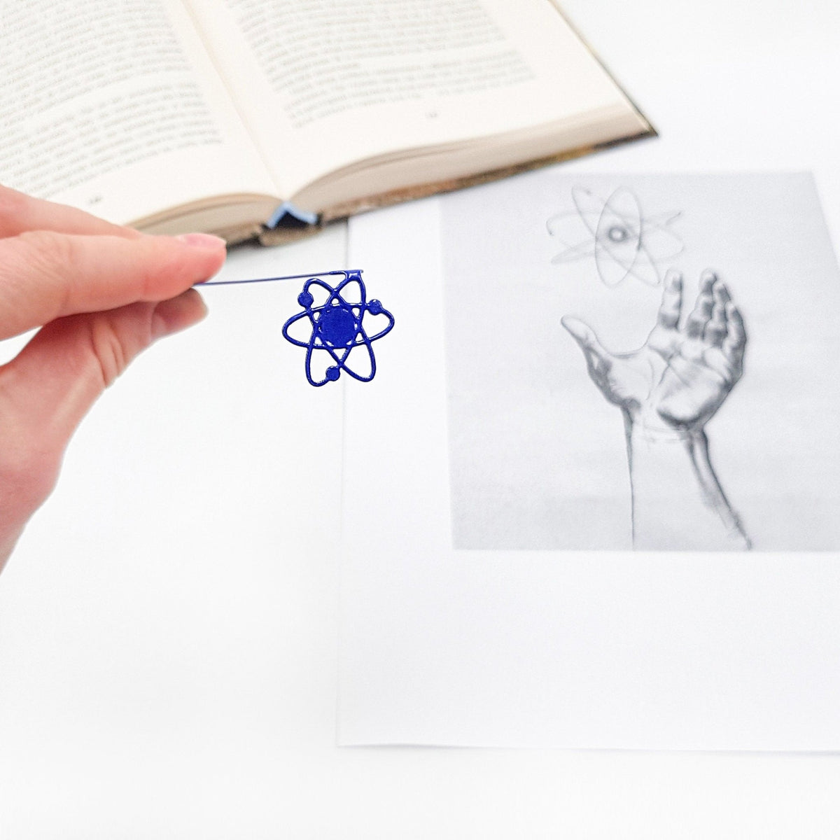 Atom metal bookmark marking a page in an illustrated book, view 4
