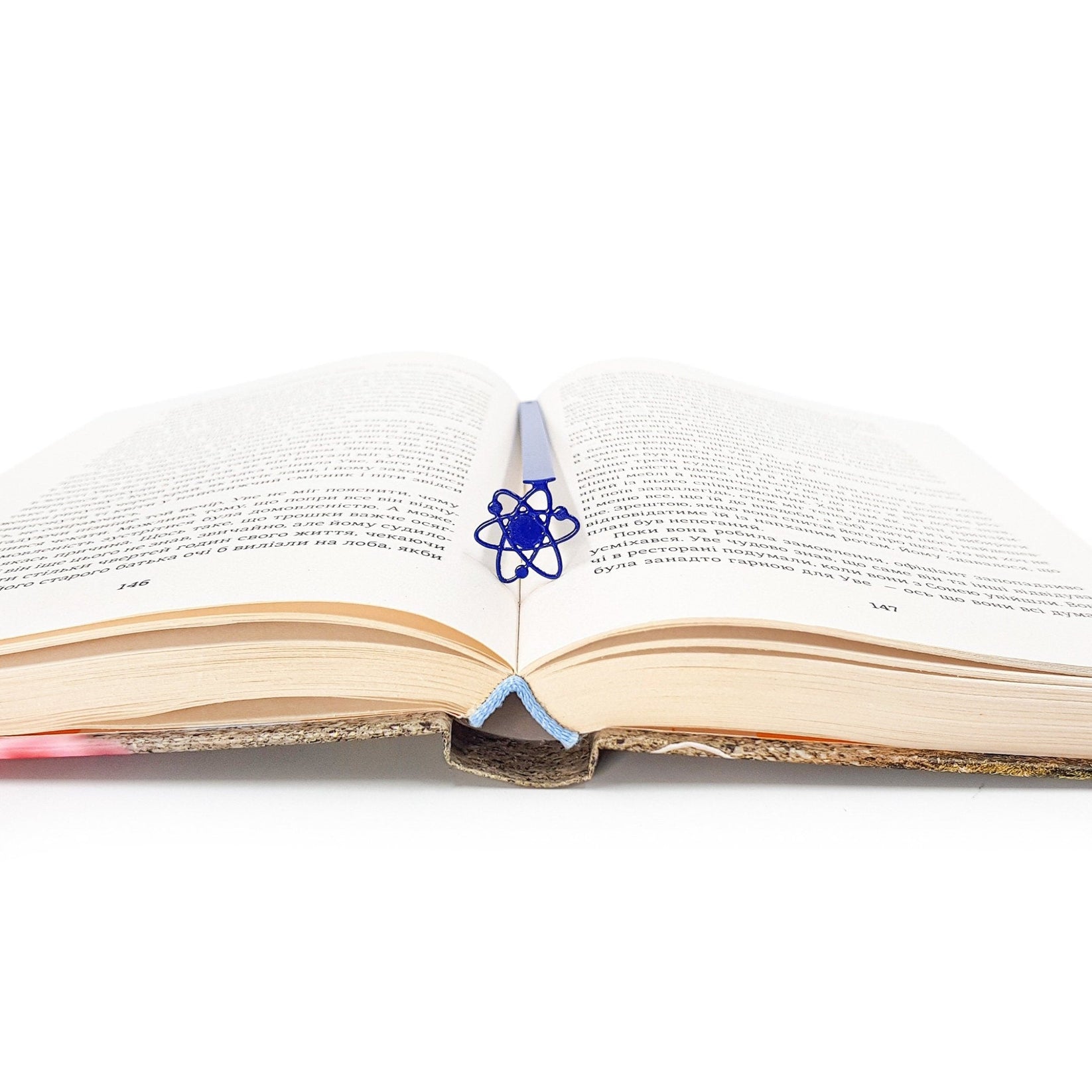 Atom metal bookmark in blue resting on the pages of an open book
