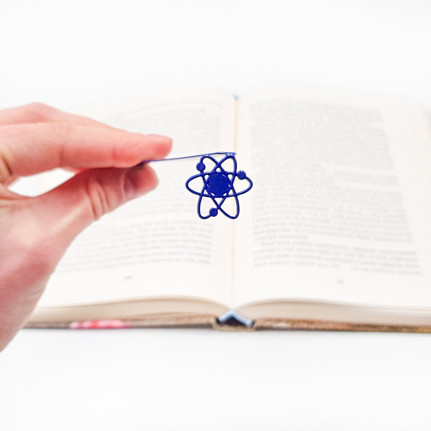 Atom metal bookmark in blue held in a hand above an open book