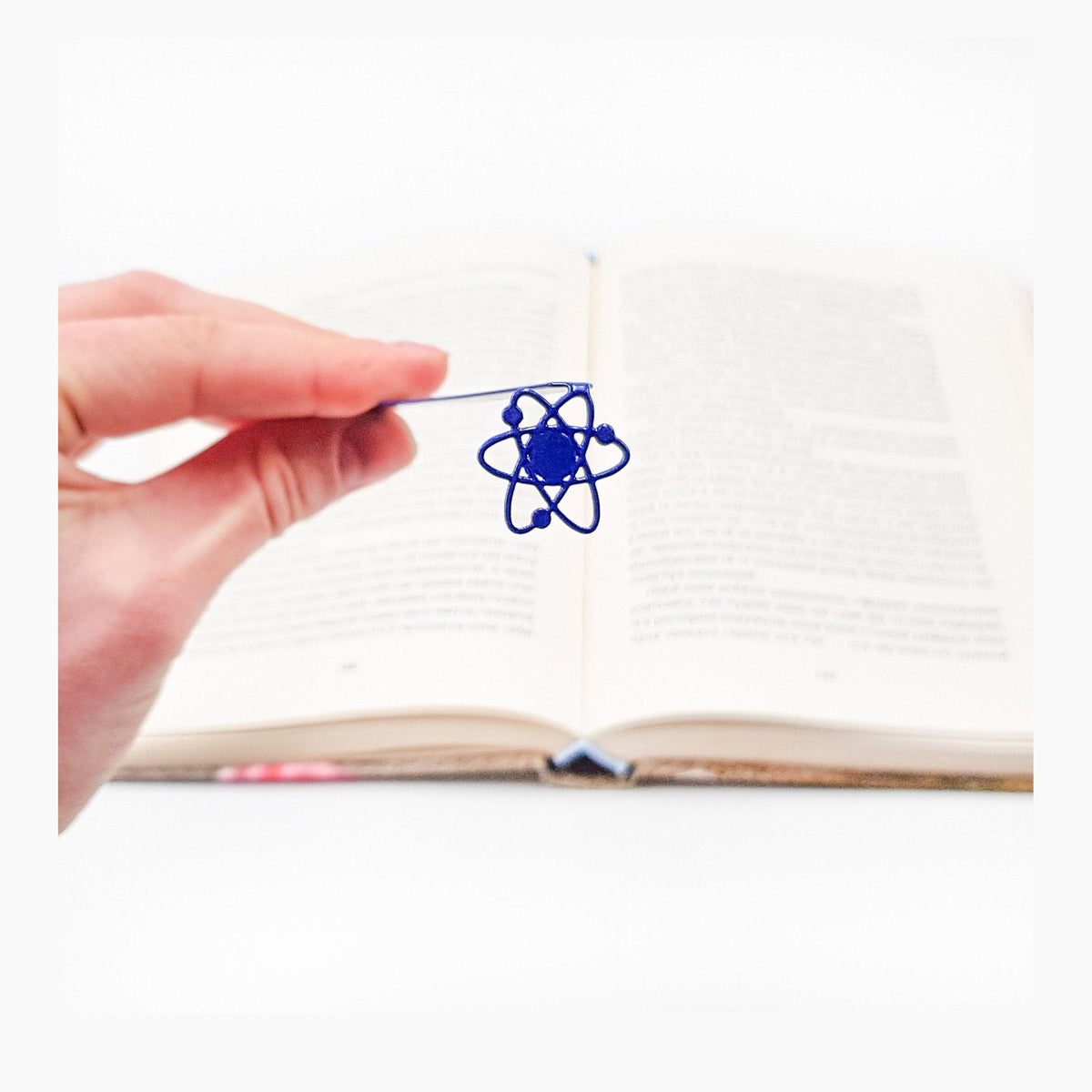 Atom metal bookmark in blue held in a hand above an open book