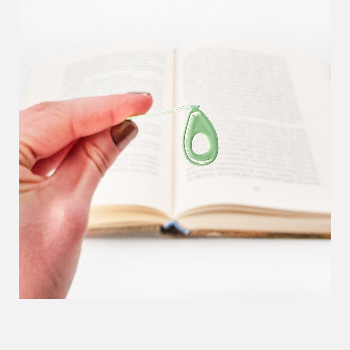 Avocado metal bookmark in green held in a hand above an open book