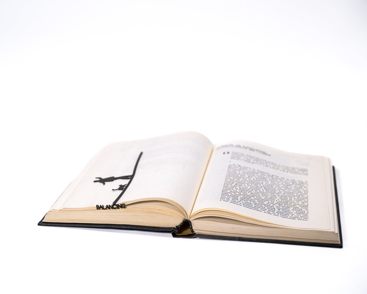 Balancing Act metal bookmark marking a page in an open book