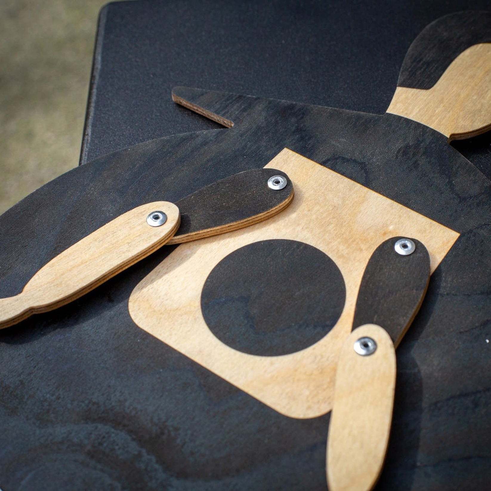 Macro close-up of the Beetle puppet's riveted arm joints and black body over natural plywood grain