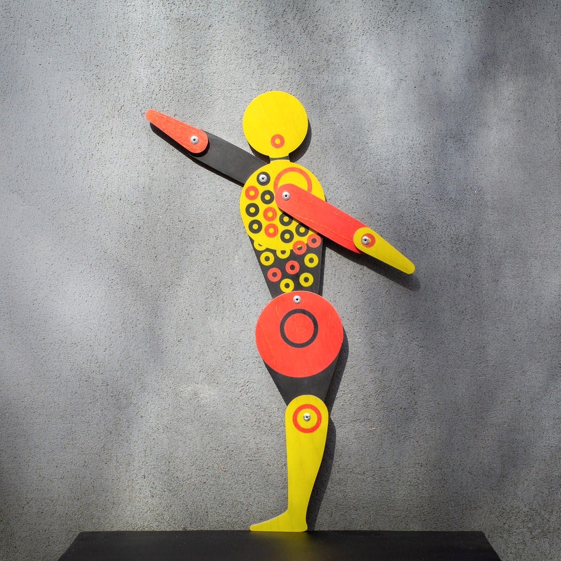 Bauhaus circle dancer puppet on grey wall with arms extended, casting dramatic shadow