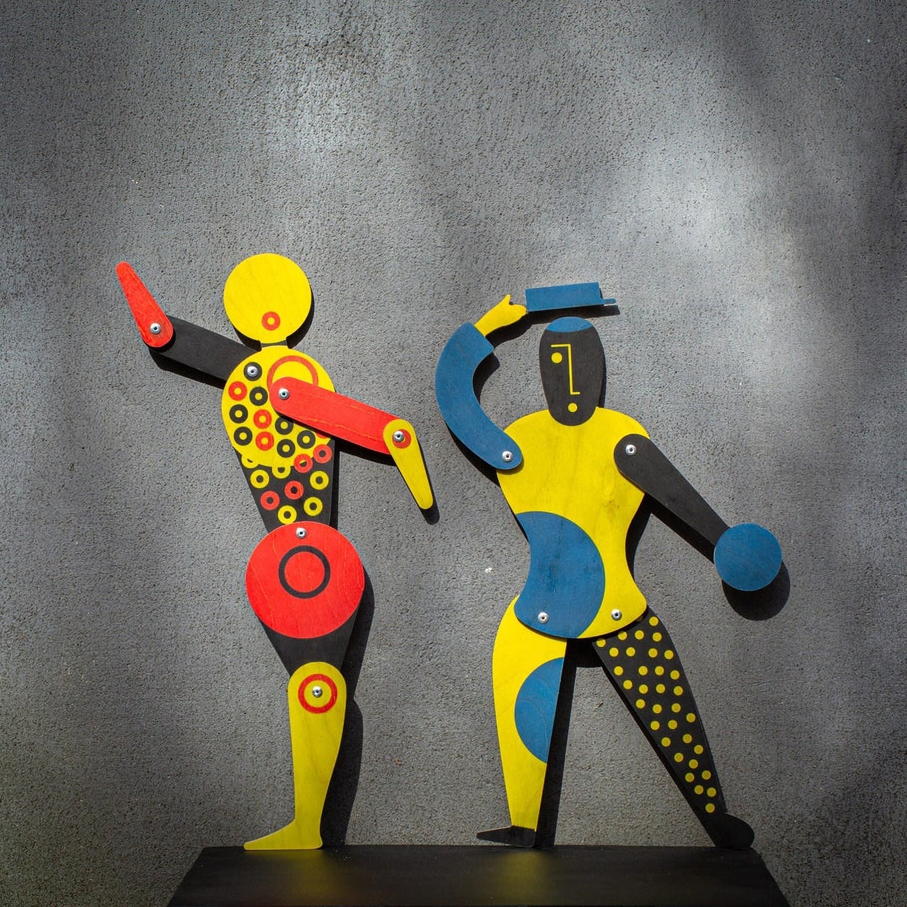 Bauhaus circle dancer puppet with blue and yellow Bauhaus companion puppet on grey wall