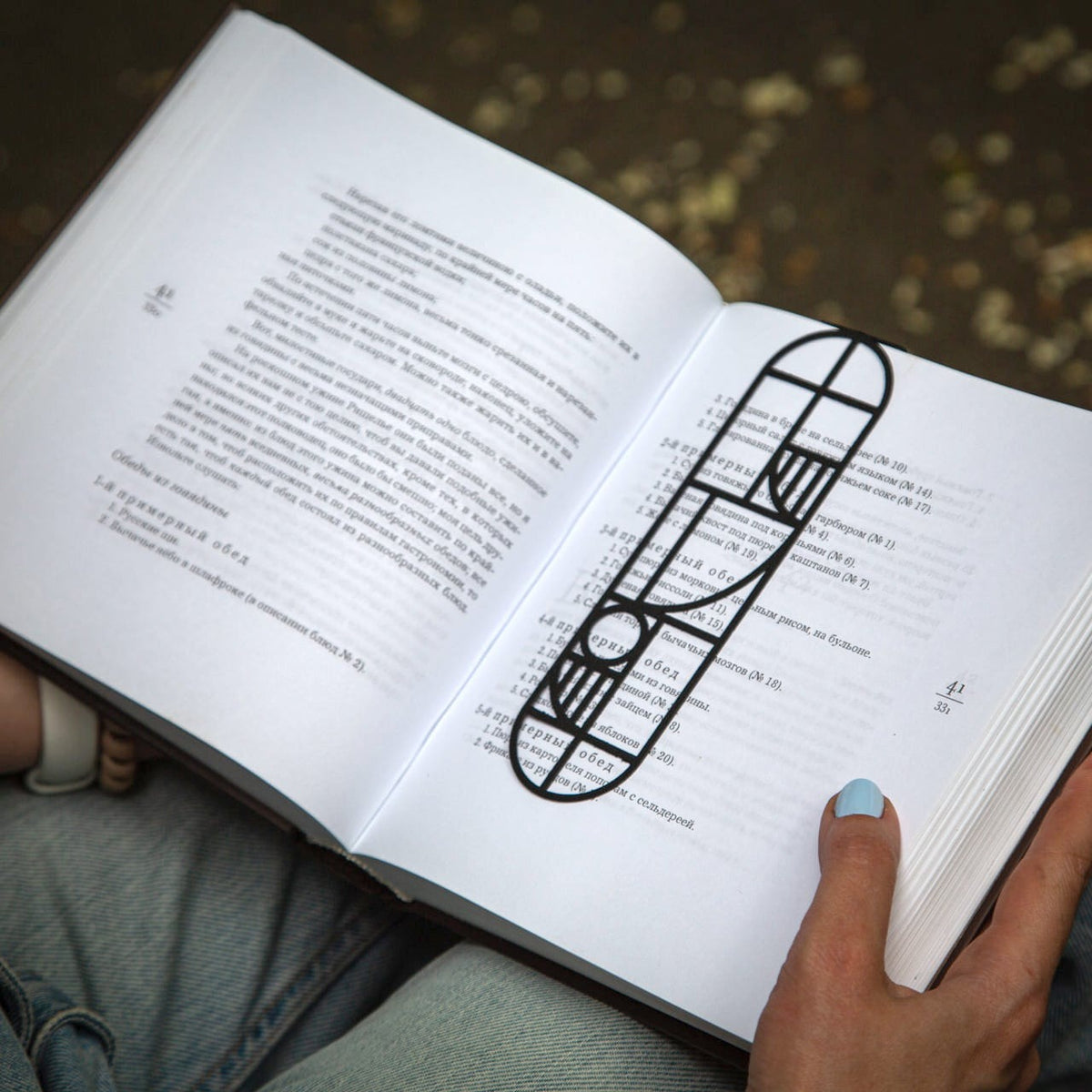 Bauhaus Geometry metal bookmark held in a hand above an open book