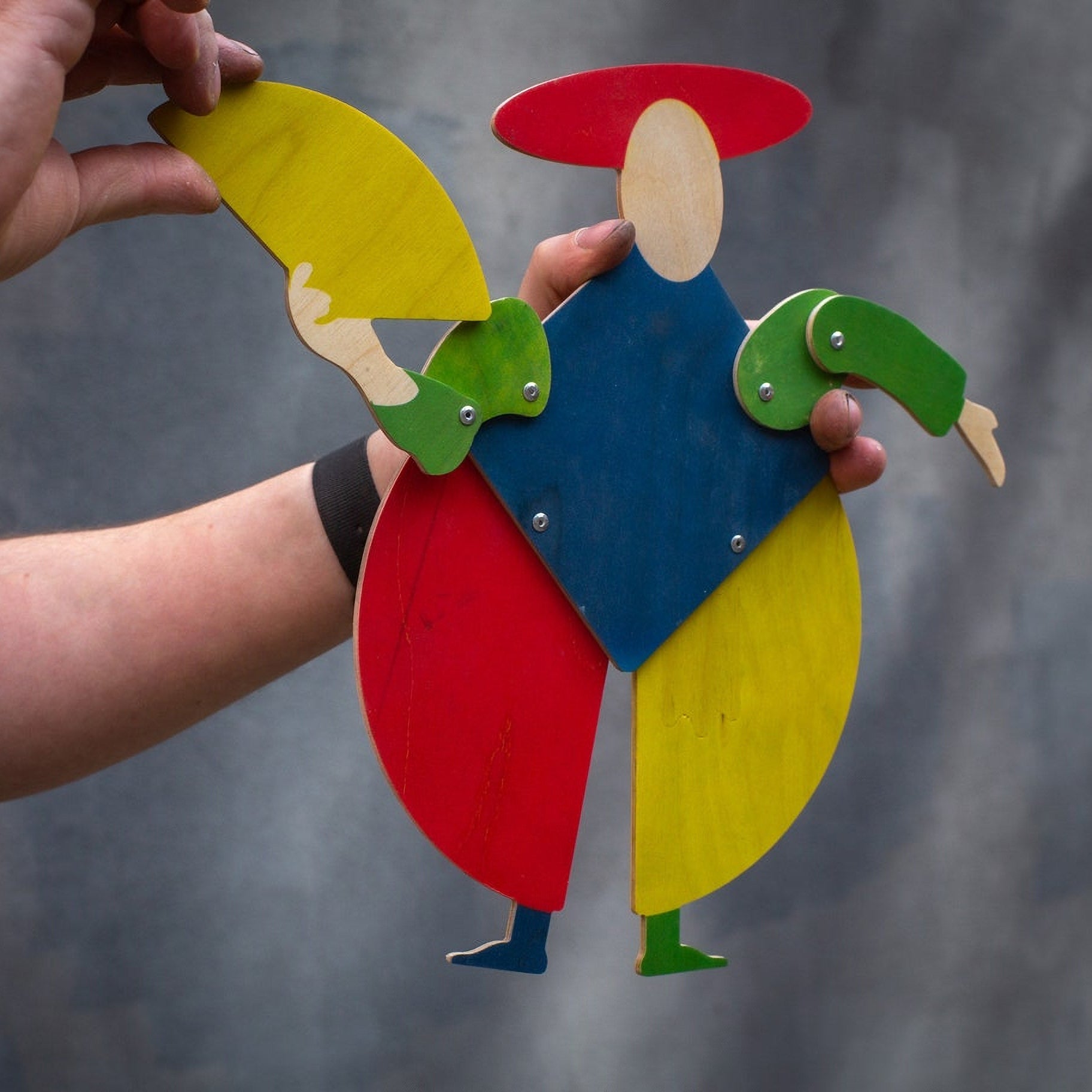 Hands posing Bauhaus harlequin puppet mid-air, showing movable joints and plywood layers