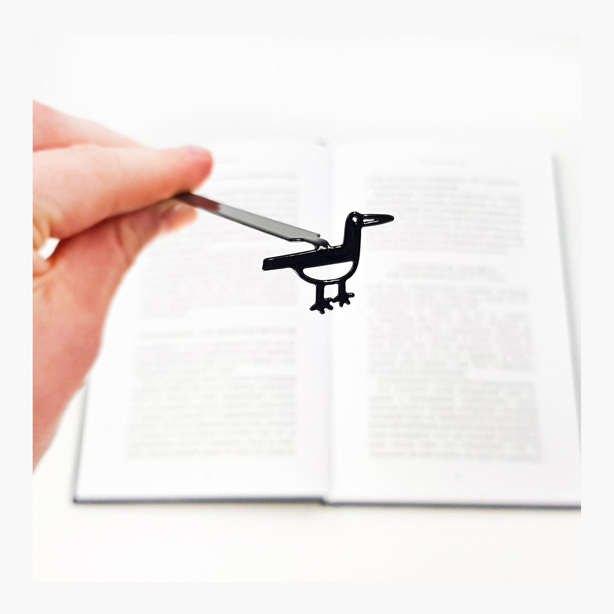 Minimalist Bird metal bookmark held in a hand above an open book