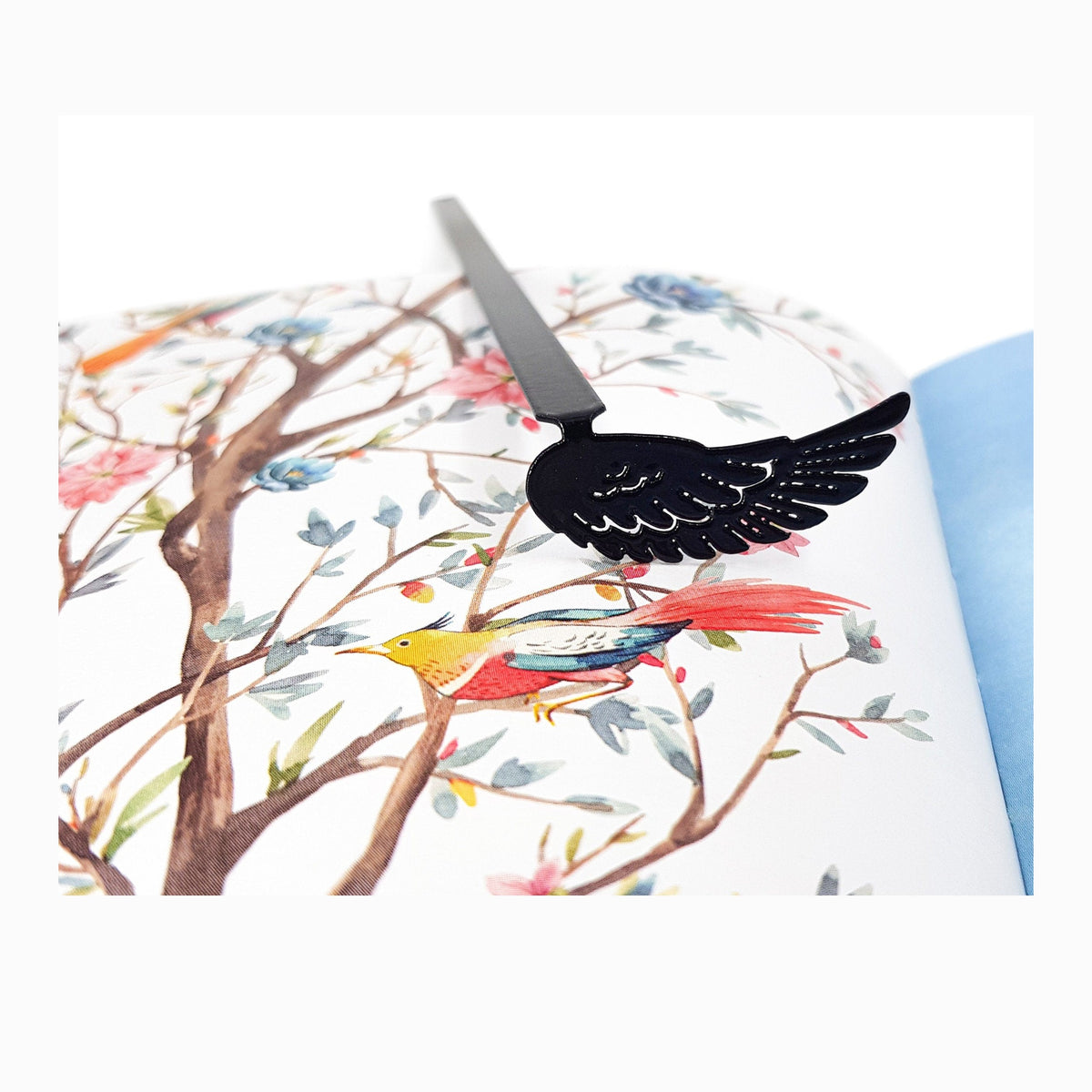 Black Wing metal bookmark marking a page in an illustrated book