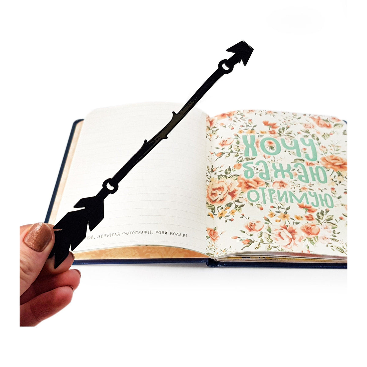 Boho Arrow metal bookmark held in a hand above an open book