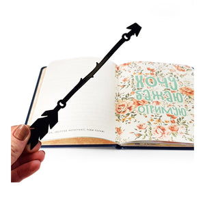 Boho Arrow metal bookmark held in a hand above an open book