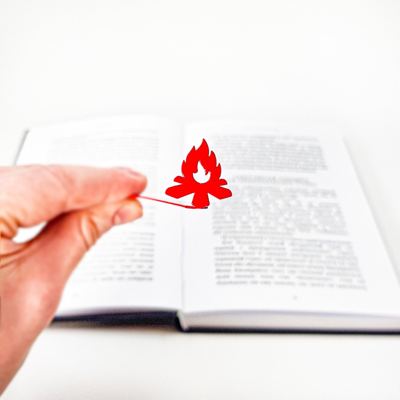 Bonfire metal bookmark in red held up beside an open book
