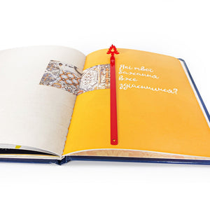 Red bonfire metal bookmark placed vertically in open book on yellow page, slim steel page marker with minimalist flame design